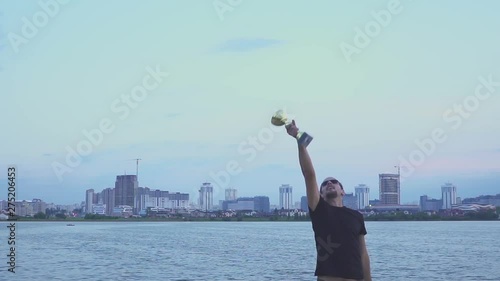 A young man with a cup in his hands rejoices in sports victory on background of the evening Minsk. Concept as victory, success and champion in sport. Slow motion.