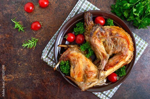 Whole baked rabbit with greens and tomatoes on a plate. Tasty dietary meat. Top view, flat lay.
