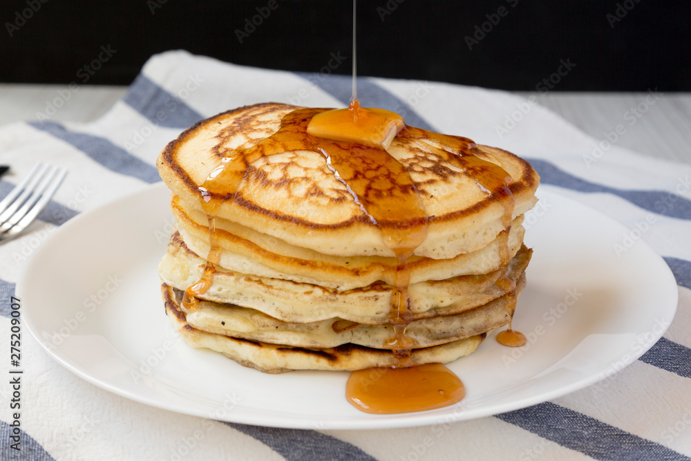 Homemade pancakes with butter and maple syrup on a white plate, side view. Close-up.