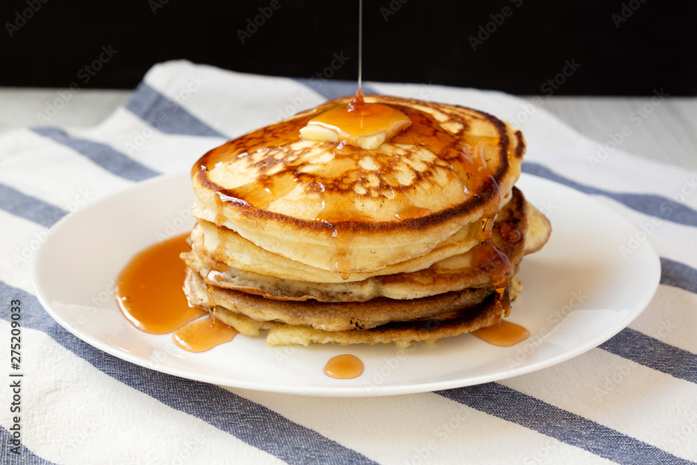 Homemade pancakes with butter and maple syrup on a white plate, side view. Closeup.