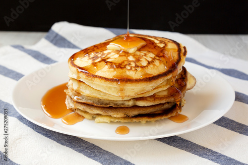 Homemade pancakes with butter and maple syrup on a white plate, side view. Closeup.