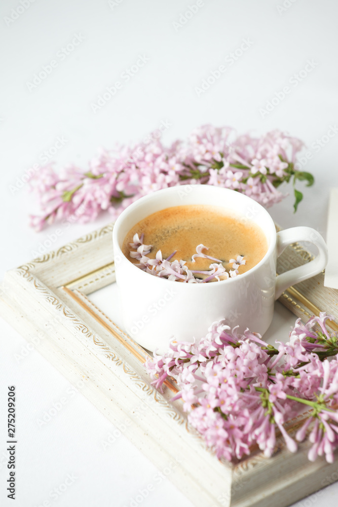 Modern still life with lilac flowers, frame and cup of coffee, on white wbackground, copy space. Holiday or wedding background. minimalist style, female breakfast