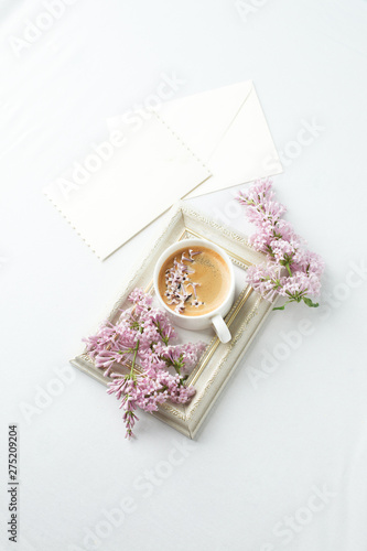 Modern still life with lilac flowers, frame and cup of coffee, on white wbackground, copy space. Holiday or wedding background. minimalist style, female breakfast