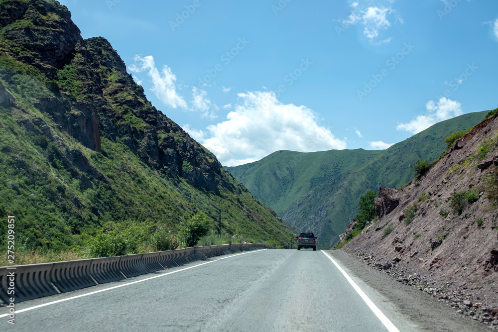 The car is driving along the road between the picturesque green hills. Travel in Kyrgyzstan