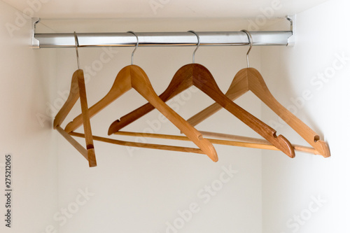 horizontal detail view of an empty metal coatrack in a white wardrobe with four empty wooden coathangers photo