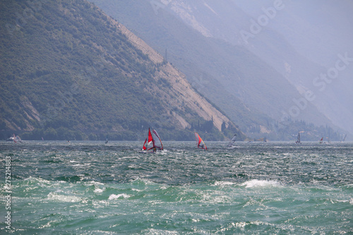 Windsurfers and sailing boats at Lake Garda glistening in the sun (Torbole, Italy)