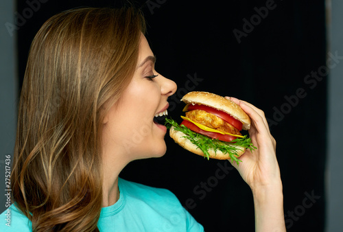young woman biting burger on black background.