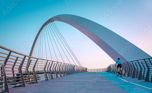Fototapeta Naklejka Na Ścianę i Meble -  Young man riding bicycle through Dubai water canal bridge, Beautiful Architecture Design