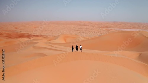 Cinematic drone shot of three friends standing on a top of sand dune in a desert photo