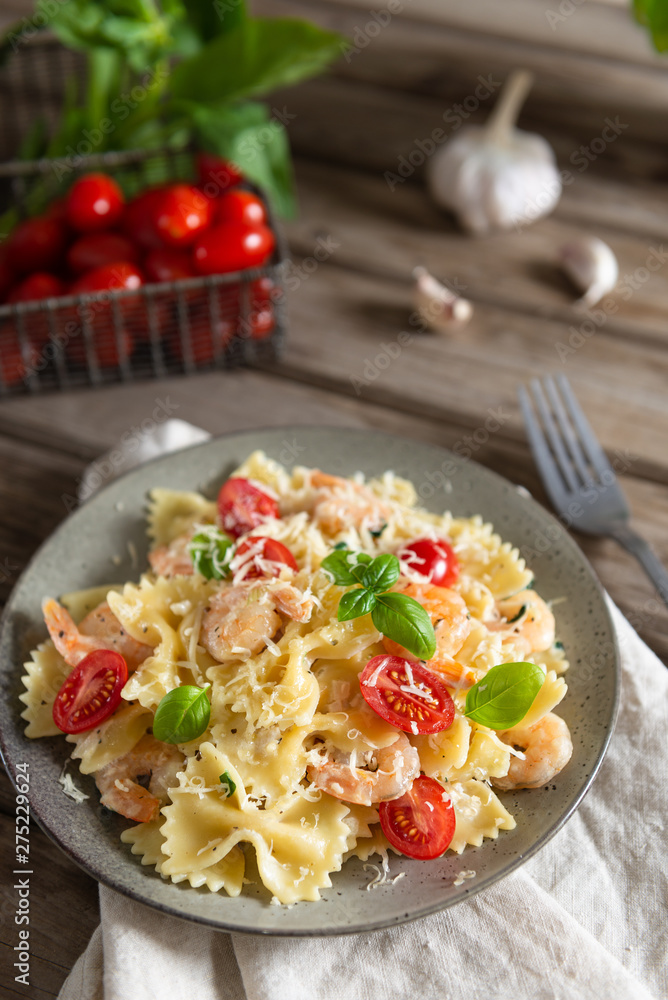 Pasta farfalle with shrimps, garlic sauce, cherry tomatoes and basil leaf on wooden table, italian cuisine, side view. Close up