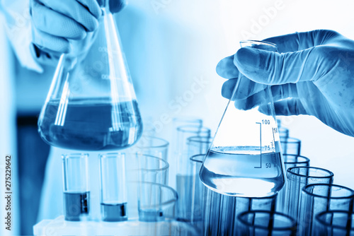hand of scientist holding flask with lab glassware and test tubes in chemical laboratory background, science laboratory research and development concept photo