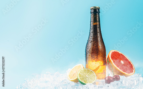 closed bottle of brown glass beer on ice. fruits lie nearby. concept of fruit craft beer or cider