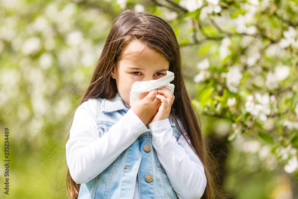 Little girl is blowing her nose near spring tree in bloom Little girl is blowing her nose near spring tree in bloom