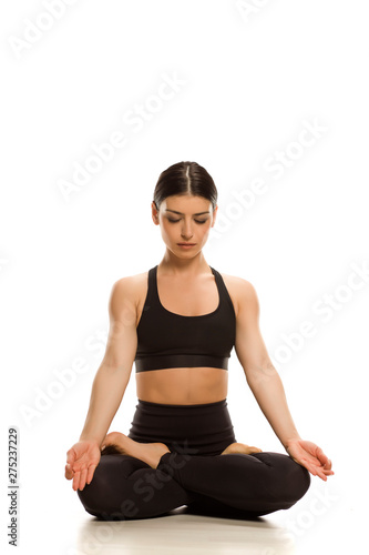 Young woman siting in lotus yoga position meditating on white background