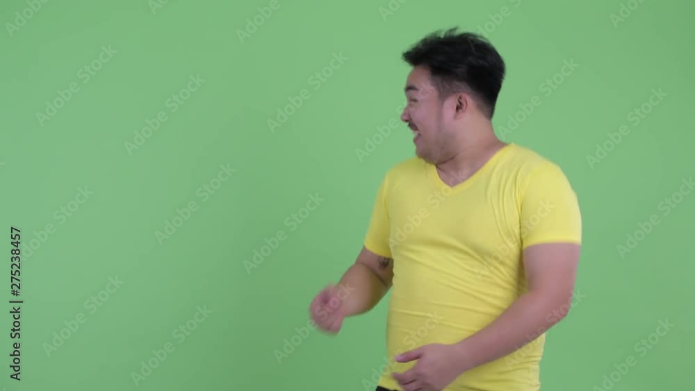 Happy young overweight Asian man touching something and looking surprised Happy young overweight Asian man touching something and looking surprised