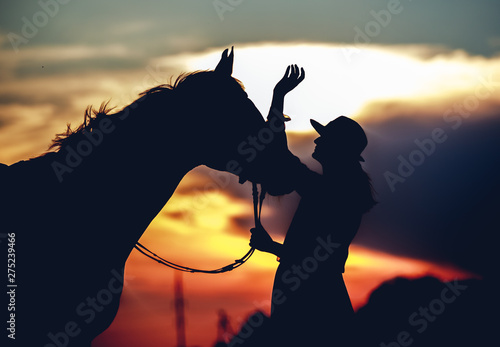 Silhouette of a girl in a hat with a horse at sunset