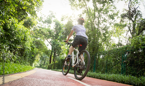 Woman cyclist riding a bike on sunny park trail in summer