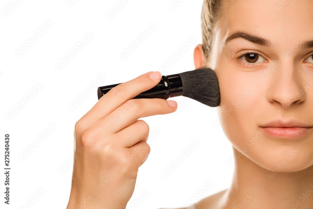 Portrait of young woman applying powder foundation with brush on white background Portrait of young woman applying powder foundation with brush on white background