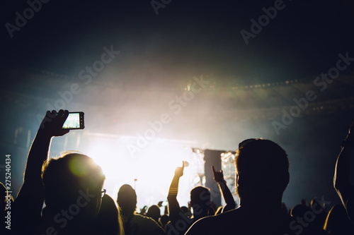 The bright spotlight shines on the dancing people. The audience applauds the musicians. Silhouette of a concert crowd.