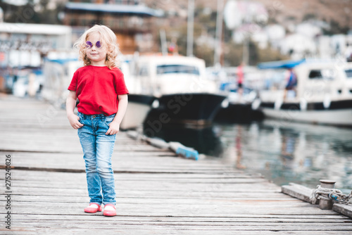 Smiling baby girl 3-4 year old standing at sea pier outdoors. Looking at camera. Summer season. © morrowlight