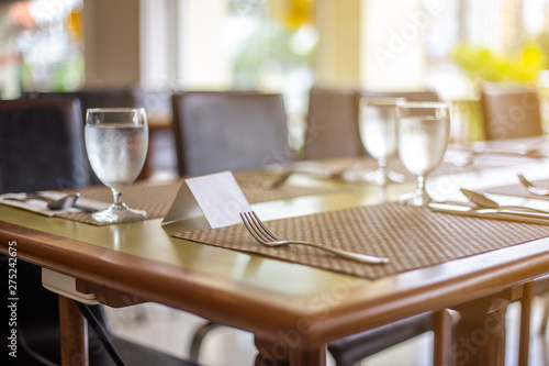 The tables and chairs in the restaurant with full set preparation next to the window with flare in the afternoon. 