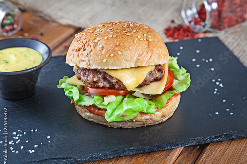 Fresh tasty burger with cheese  lettuce  tomato  cucumber on black stone with sauce. American fast food. Cheeseburger with copy space on wooden background. Close up  selective focus. Food. Grill menu