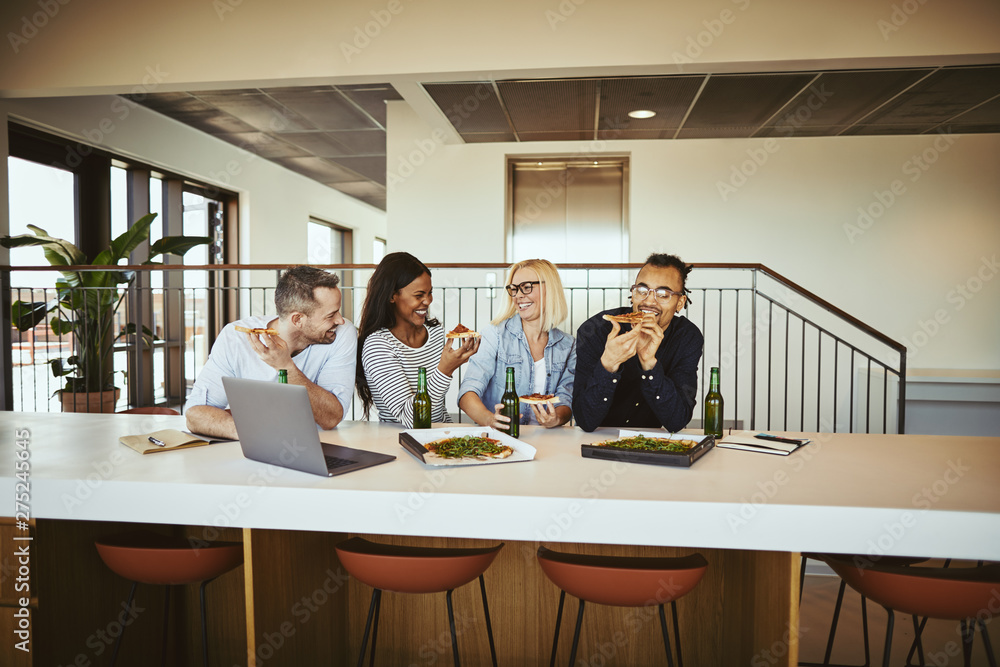 Obraz premium Laughing coworkers having pizza and beer after work