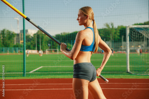 Professional female pole vaulter training at the stadium in sunny day. Fit female model practicing in high jumps outdoors. Concept of sport, activity, healthy lifestyle, action, movement, motion.