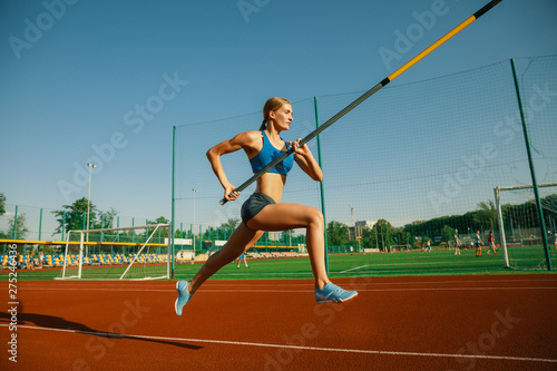 Professional female pole vaulter training at the stadium in sunny day. Fit female model practicing in high jumps outdoors. Concept of sport, activity, healthy lifestyle, action, movement, motion.