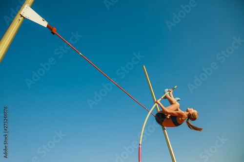 Professional female pole vaulter training at the stadium in sunny day. Fit female model practicing in high jumps outdoors. Concept of sport, activity, healthy lifestyle, action, movement, motion. photo