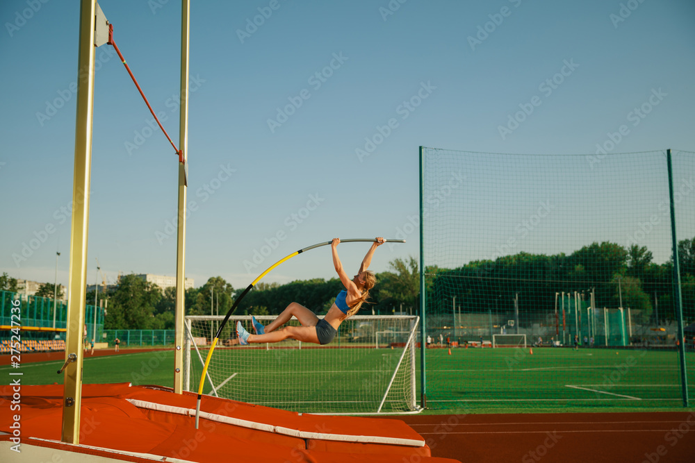 Professional female pole vaulter training at the stadium in sunny day. Fit female model practicing in high jumps outdoors. Concept of sport, activity, healthy lifestyle, action, movement, motion.