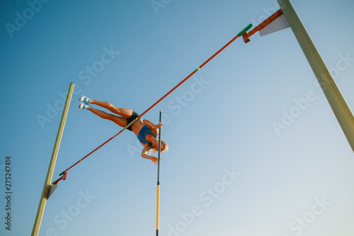 Professional female pole vaulter training at the stadium in sunny day. Fit female model practicing in high jumps outdoors. Concept of sport, activity, healthy lifestyle, action, movement, motion.