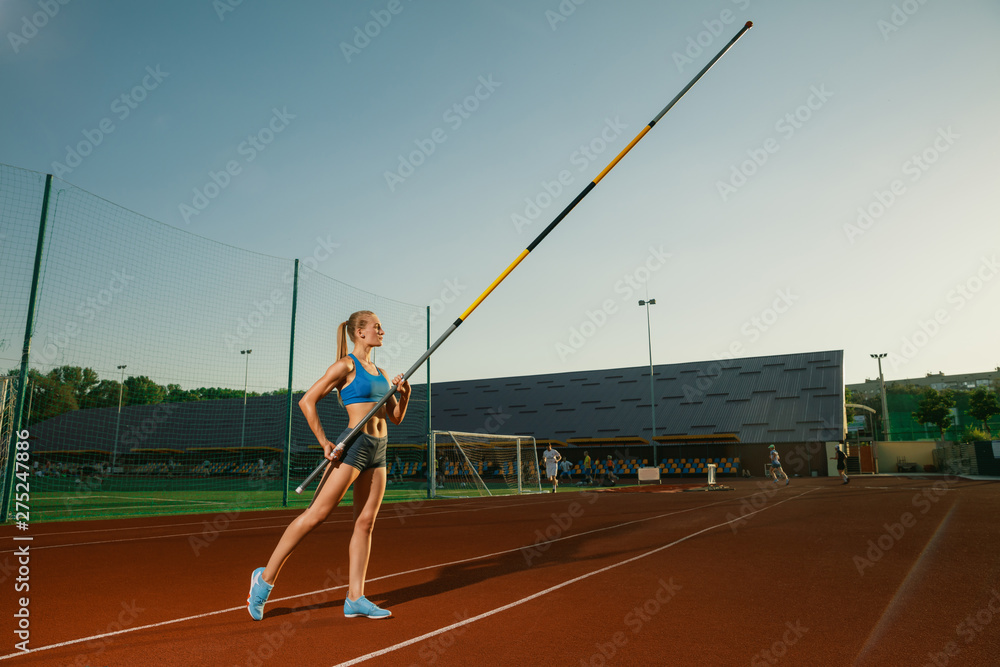 Professional female pole vaulter training at the stadium in sunny day. Fit female model practicing in high jumps outdoors. Concept of sport, activity, healthy lifestyle, action, movement, motion.