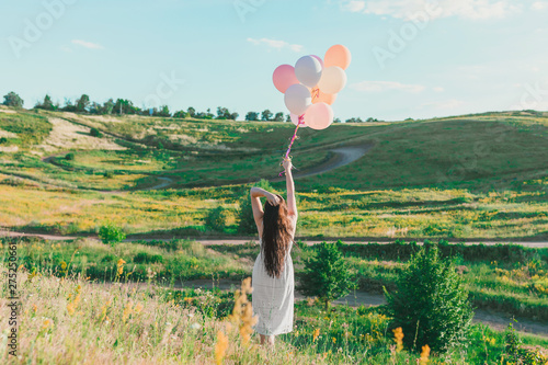 The girl holds a bunch of colorful balloons against the background of nature. Concept - congratulations on the holiday, Birthday