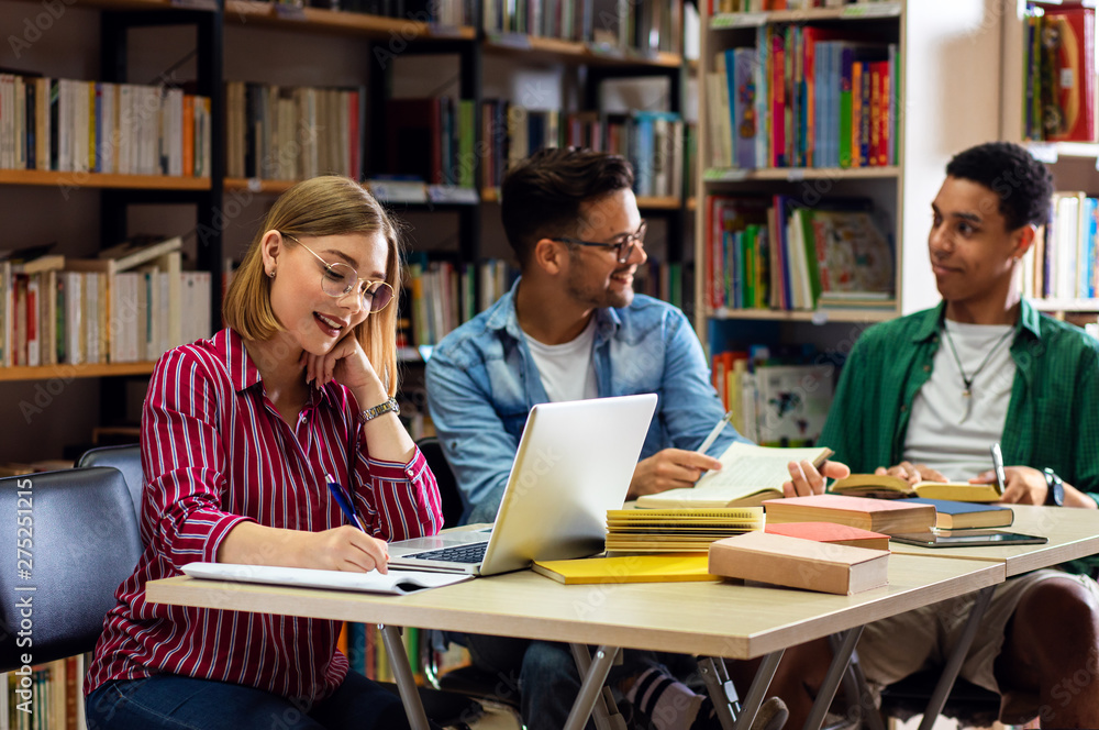 Three young students study in the school library, female student using laptop for researching online. Three young students study in the school library, female student using laptop for researching online.