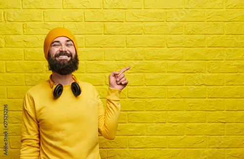 Cheerful hipster pointing at yellow wall