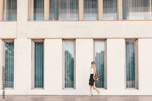 Fashionable tall business woman in sunglasses walking near a building with tall windows in the city © arthurhidden
