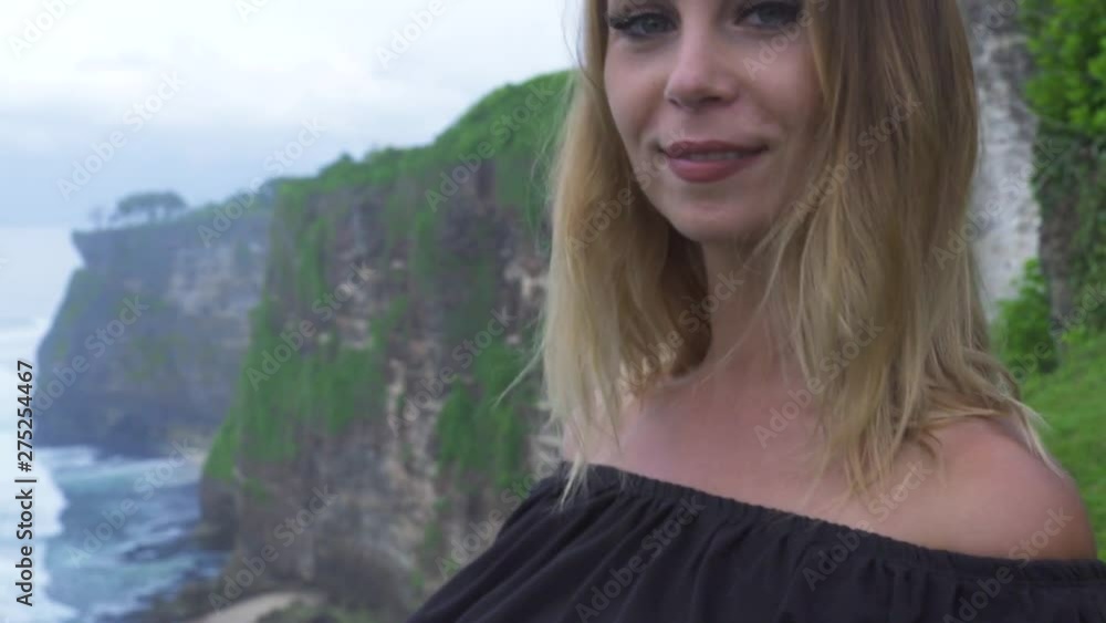 Smiling happy woman enjoying cliff mountain and water waves landscape on ocean shore. Cheerful woman on mountain cliff edge landscape and splashing sea waves. Wild nature Bali, Indonesia. Smiling happy woman enjoying cliff mountain and water waves landscape on ocean shore. Cheerful woman on mountain cliff edge landscape and splashing sea waves. Wild nature Bali, Indonesia.