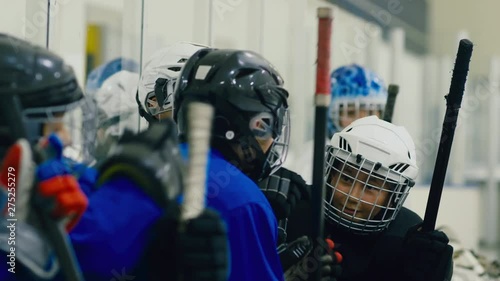 Guys in hockey uniform sitting on bench before training, talking to each other, smiling and greeting incomers