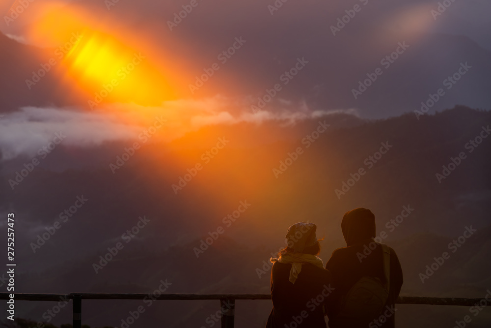 Couple looking at beautiful sunrise and layers of mountains view from camping spot at Doi pui ko, Mae hong son, Thailand.