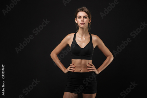 Portrait of focused caucasian woman in sportswear standing with arms on waist during workout in gym