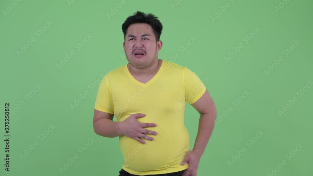 Funny young overweight Asian man having stomachache Funny young overweight Asian man having stomachache