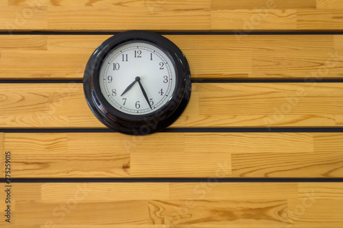 large black round clock with arrows close-up on a yellow wooden plank wall. horizontal lines. natural texture surface