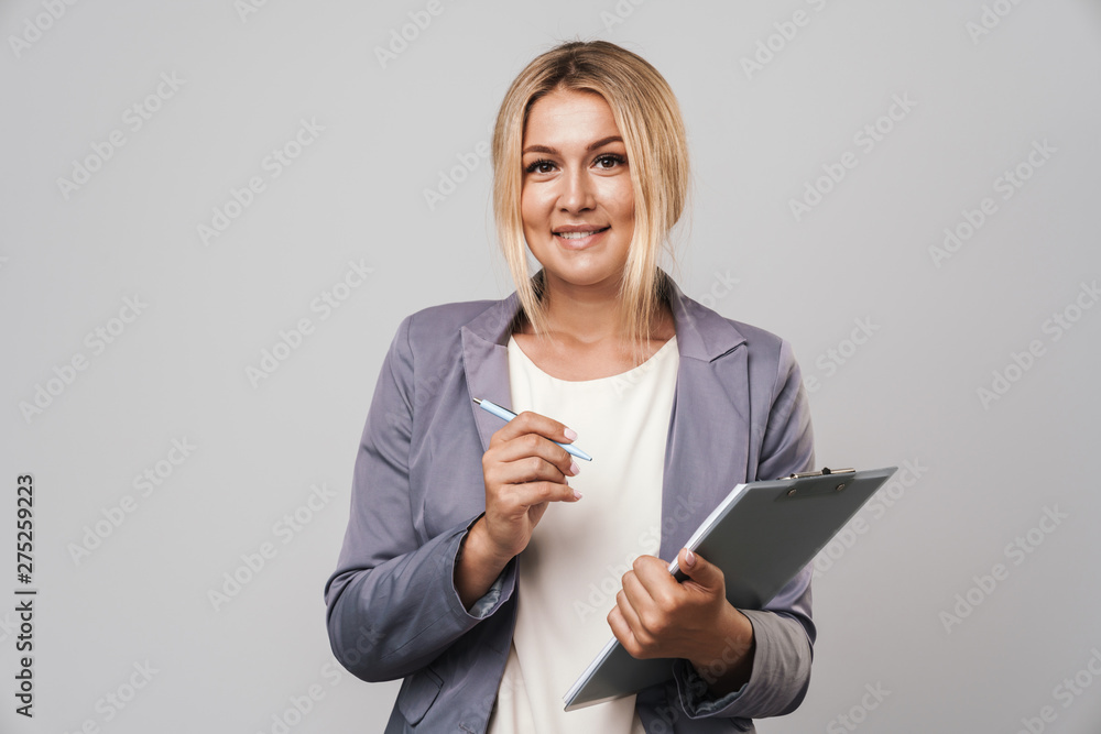 Happy young pretty woman posing isolated over grey wall background holding clipboard. Happy young pretty woman posing isolated over grey wall background holding clipboard.