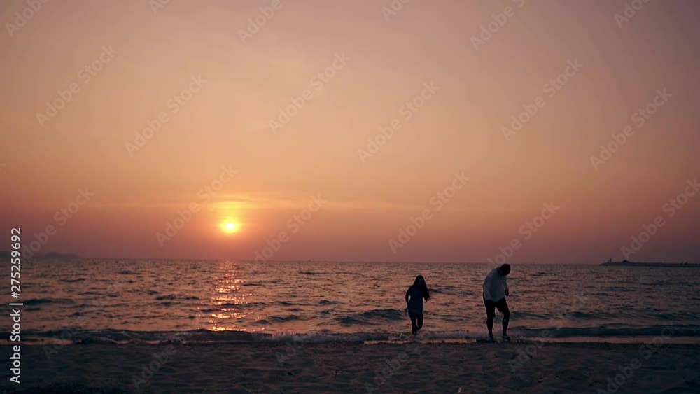 silhouettes of guy and girl going out of sea water on empty shore in early dusk against sunset slow motion silhouettes of guy and girl going out of sea water on empty shore in early dusk against sunset slow motion