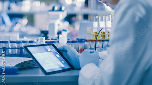 Senior Male Research Scientist is Using a Tablet Computer in a Modern High-Tech Laboratory. Genetics and Pharmaceutical Studies and Researches. photo