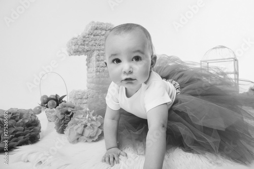 Birthday celebration: girl sitting on the floor among the numbers 1, artificial flowers and bird cage photo