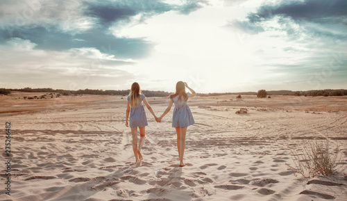 Two girls walk along the sand against the sky in the sunset