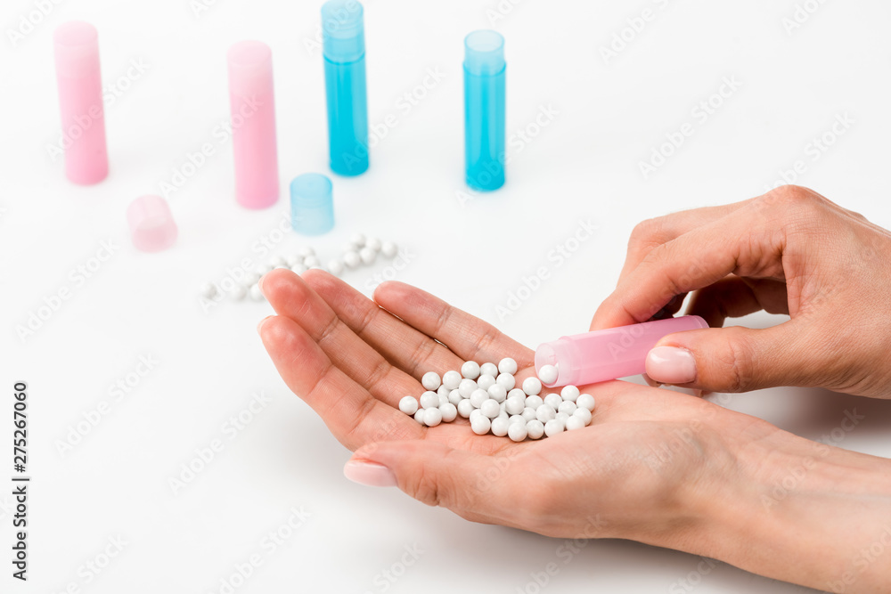 cropped view of woman holding round pills in hand near blue and pink bottles on white