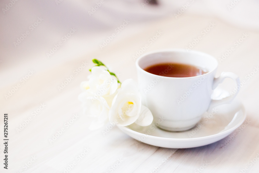 cup of tea on a saucer and a white freesia flower cup of tea on a saucer and a white freesia flower